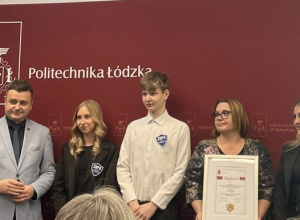 Uczniowie i pani dyrektor pozują do zdjęcia na ściance Politechniki Łódzkiej