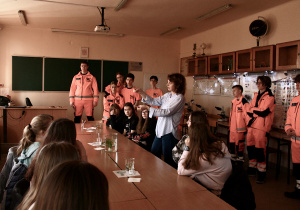 Uczniowie klasy przyrodniczej w mundurach ratowników medycznych w sali 02 w budynku ZSP 8, pokazują eksperymenty biologiczne, zaproszeni goście siedzą i słuchają