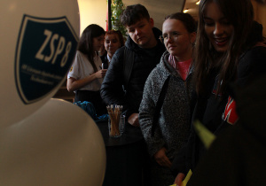 Uczniowie stoją przy stoisku promocyjnym ZSP 8 w korytarzu na parterze