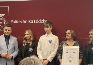 Uczniowie i pani dyrektor pozują do zdjęcia na ściance Politechniki Łódzkiej